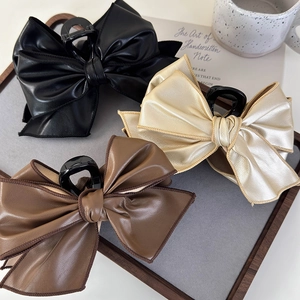 Three oversized vintage leather bow hair claws in black, gold, and brown on a wooden tray