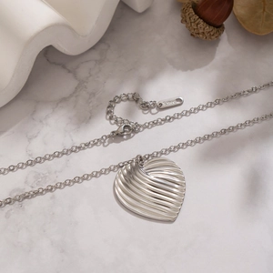 Close-up of heart pendant with wave texture and S.Steel tag on silver necklace