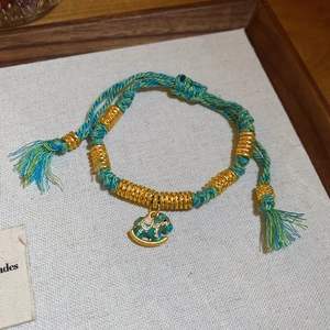 Detail of red woven bracelet with green enamel horse pendant and gold metal beads