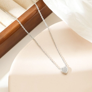 Sparkling silver heart pendant necklace with micro-paved crystals on a beige display stand