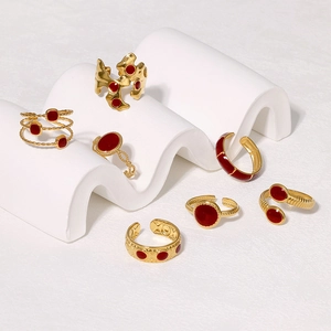 Detail of vintage gold-plated stainless steel rings with red enamel accents on a white stand