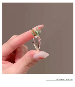 Macro shot of a pink crystal carrot brooch with green stones in gold setting held in hand