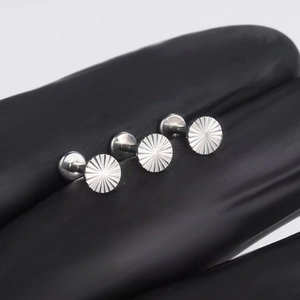 Gros plan de trois clous d'oreille en titane G23 avec motif soleil sur un gant noir