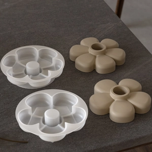 Six-petal flower resin silicone mold with khaki plaster candle base on a dark grey surface