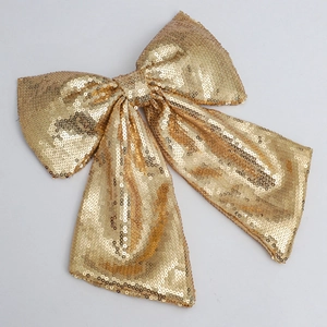 Detailed close-up of a large golden sequined Christmas bow ornament on a grey background