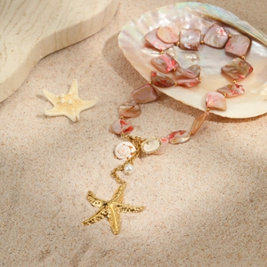 Summer ocean style necklace with pink shell beads, starfish pendant and pearls on sandy beach