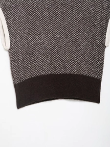 Detail of herringbone knit vest with ribbed hem and white contrast sleeve piping