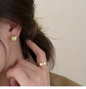 Close-up of minimalist gold beaded earrings and a wide band ring on a female model