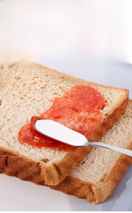 Gros plan d'un couteau à beurre en inox étalant de la confiture sur du pain grillé