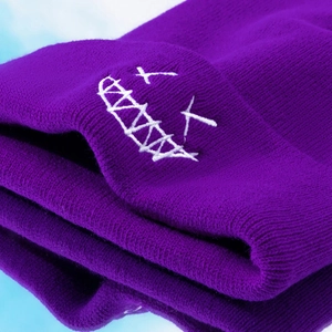 Macro shot of purple knit beanie featuring white embroidered smile face detail