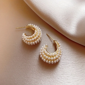 Elegant gold-tone C-shaped hoop earrings with faux pearl inlay on silk background