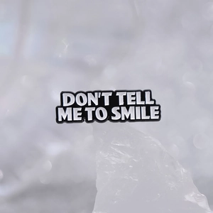 Minimalist geometric metal brooch featuring white Don't Tell Me To Smile text on black enamel