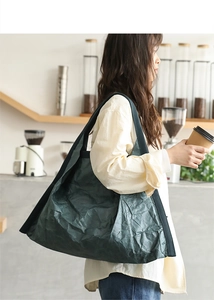 Detail shot of green tote bag in Dupont paper fabric on model in a cozy cafe setting