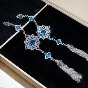 Detailed macro of silver long tassel earrings with blue pear-shaped gemstones on black velvet