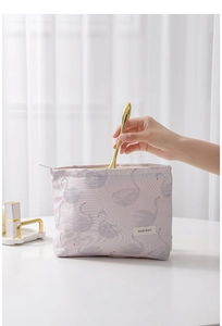 Pink swan jacquard cosmetic bag with zipper and logo tag being filled with beauty tools