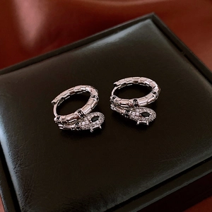Detailed macro of silver snake hoop earrings with zircons on a black leather box