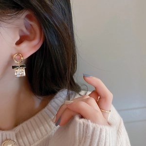 Boucles d'oreilles dorées élégantes avec nœud noir et cristal carré portées par modèle
