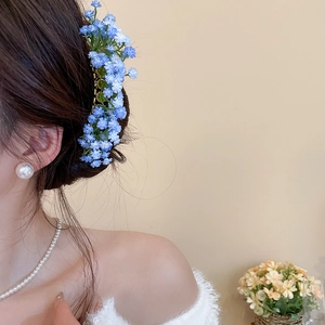 Detailed side view of a blue and purple floral hair clip worn by a model in warm light