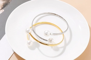 Detailed view of gold and silver minimalist open pearl bracelets on a ceramic plate