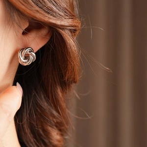 Close-up of a silver twisted knot stud earring worn on a model's earlobe