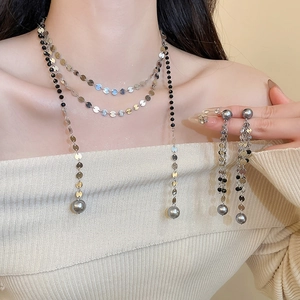 Detail of layered necklace and tassel earrings with silver discs and grey pearls