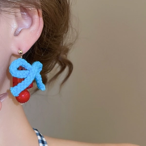 Close-up of blue bow earrings with red geometric resin charms worn on earlobe