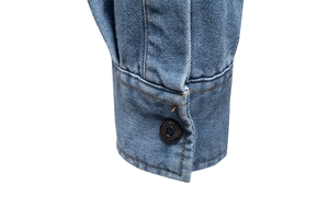 Detailed macro view of the single-button denim cuff and stitching on a blue cotton shirt