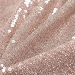 Macro shot of shimmering sequins on nude pink mesh fabric with soft glowing texture