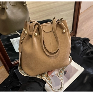 Detail of khaki lychee leather bucket bag featuring a patterned wide shoulder strap