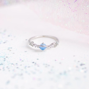 Macro shot of silver Saturn ring with light blue stone and zircon on a glittery background