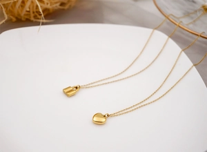 Détail des pendentifs cœur et cadenas dorés sur des chaînes fines sur céramique blanche