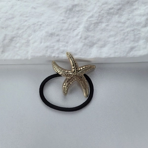Detail of a golden metal starfish charm on a high-elasticity black hair tie for ponytails
