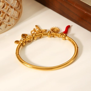 Gold-plated stainless steel bangle featuring red enamel chili and sun charms on a white table