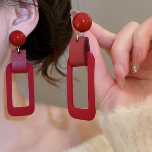 Macro detail of red rectangular flocking drop earrings worn on ear showing texture