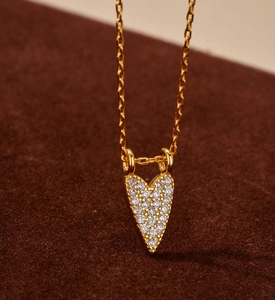 Macro shot of gold heart pendant necklace with pave white stones on brown velvet