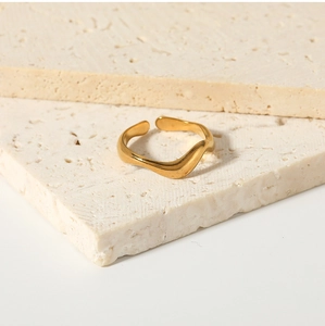 Macro detail of wave-shaped stainless steel gold ring on minimalist stone background