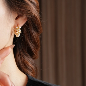 Detailed view of gold cluster pearl earrings with zircons worn on a female model