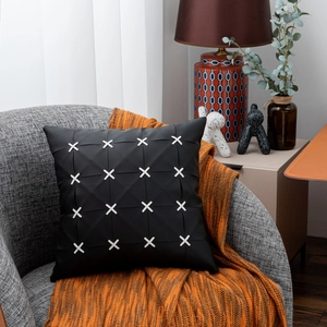 Detail of black leather pillowcase featuring white X-shaped stitching on a grey chair