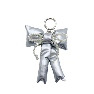 Silver metallic bow keychain with white pearls on a minimalist white background