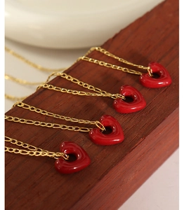 Detail of four golden necklaces featuring glossy red heart-shaped pendants on wood