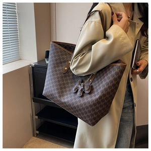 Detail of coffee brown tote bag with monogram print and cute doll pendant accessory