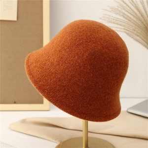 Detailed close-up of rust red knitted bucket hat with thick wool texture on a gold stand