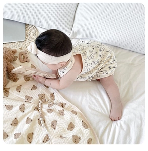 Close-up of a beige cotton gauze baby blanket featuring cute bear patterns in a home setting