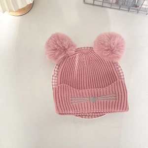 Close-up of pink knit baby hat featuring fluffy double pom-poms and silver cat embroidery