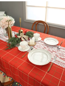 Detail of red checkered tablecloth with white lace runner and elegant holiday table setting