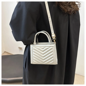 Silver chevron quilted handbag with gold hardware worn as a crossbody bag by a model