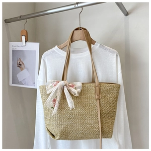 Detail of hand-woven straw tote bag with white lace floral bow and brown leather handles