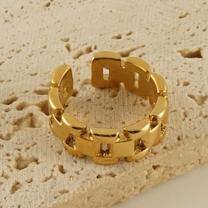 Detail of gold geometric chain ring on beige stone background showing thick metal texture