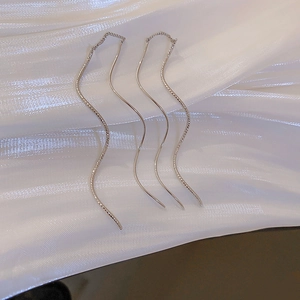 Detailed view of silver wavy S-shape long tassel earrings on white silk fabric