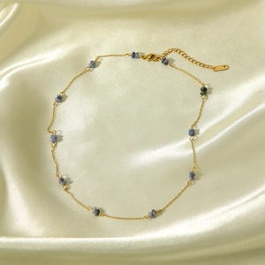 Macro view of gold stainless steel necklace chain with blue stone beads and logo tag